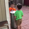 Kids take turns to play each other with the garbage can cover